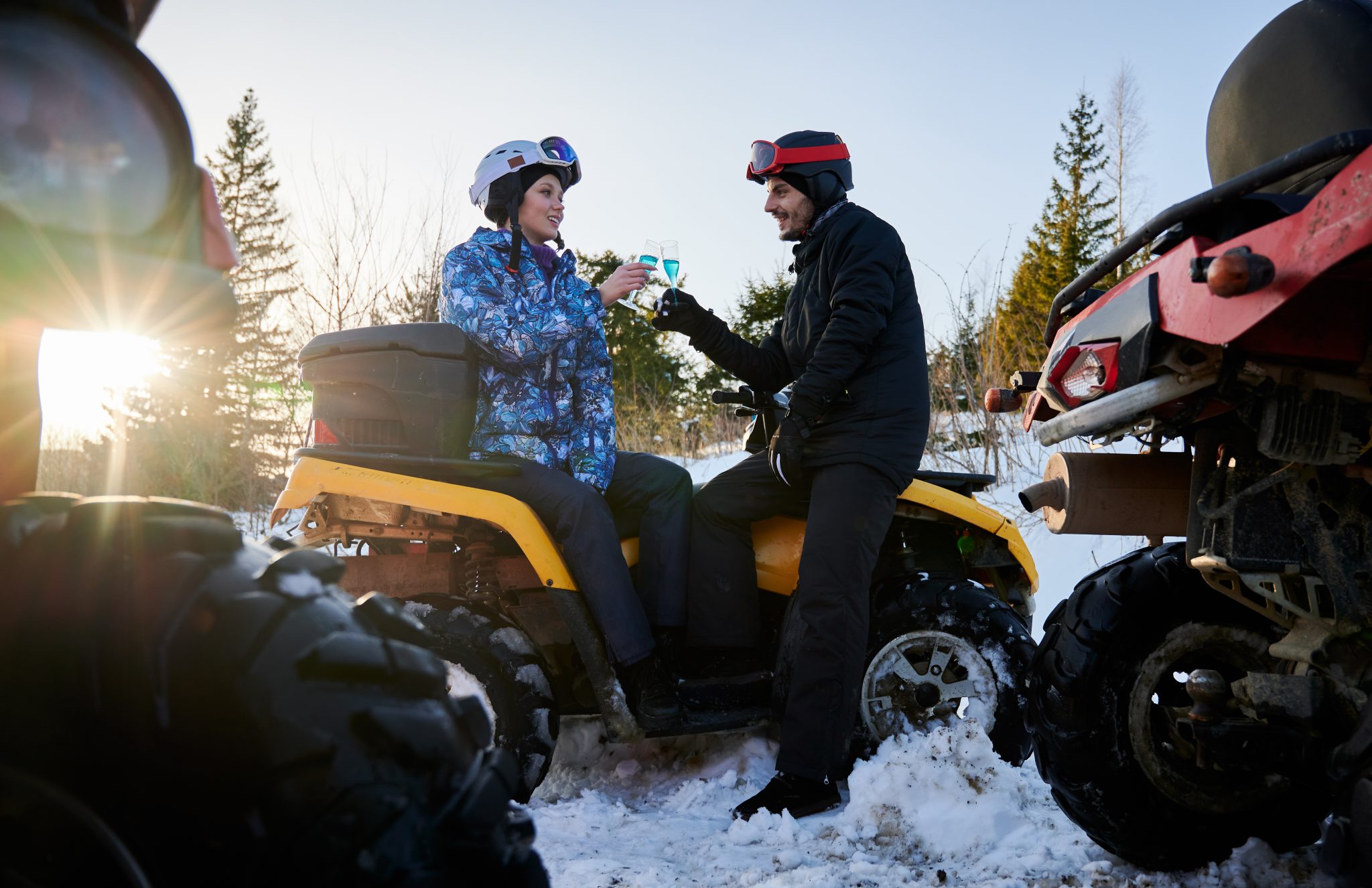 romantic couple outdoor winter celebrating with blue champagne sitting yellow atv scaled